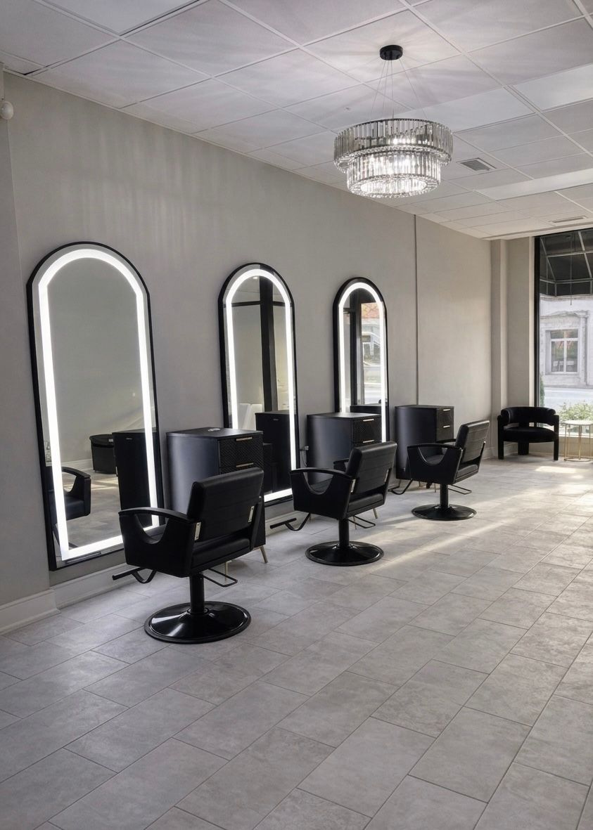 Modern salon interior with black styling chairs, arched windows, tiled floor, and a chandelier.