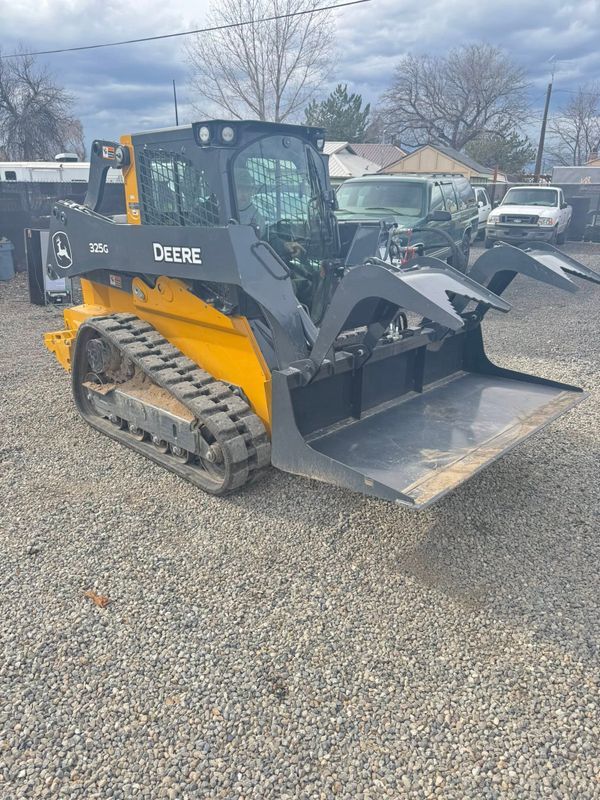 Yellow and black John Deere skid steer loader parked on gravel with bucket attachment￼