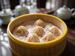 Steamed dumplings in a bamboo basket on a table, with a teapot blurred in the background