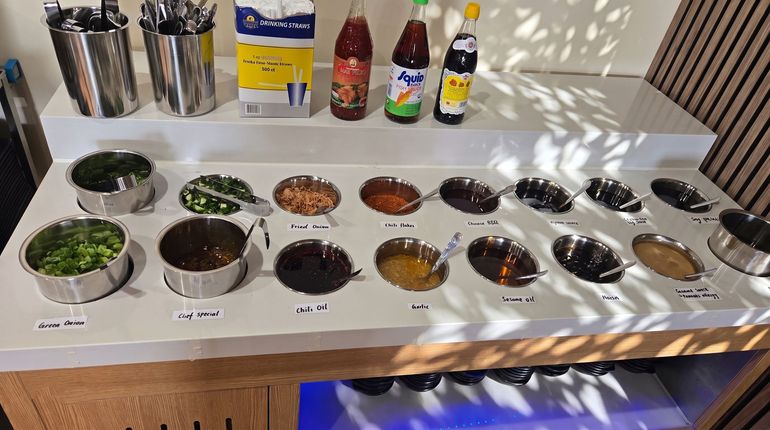 Sauce tasting setup with many small bowls of herbs and condiments on a white table