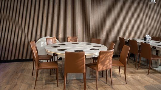 Modern dining room with round tables, wooden chairs, and a ribbed wood wall backdrop