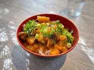 Red bowl of diced food topped with green herbs on a gray table