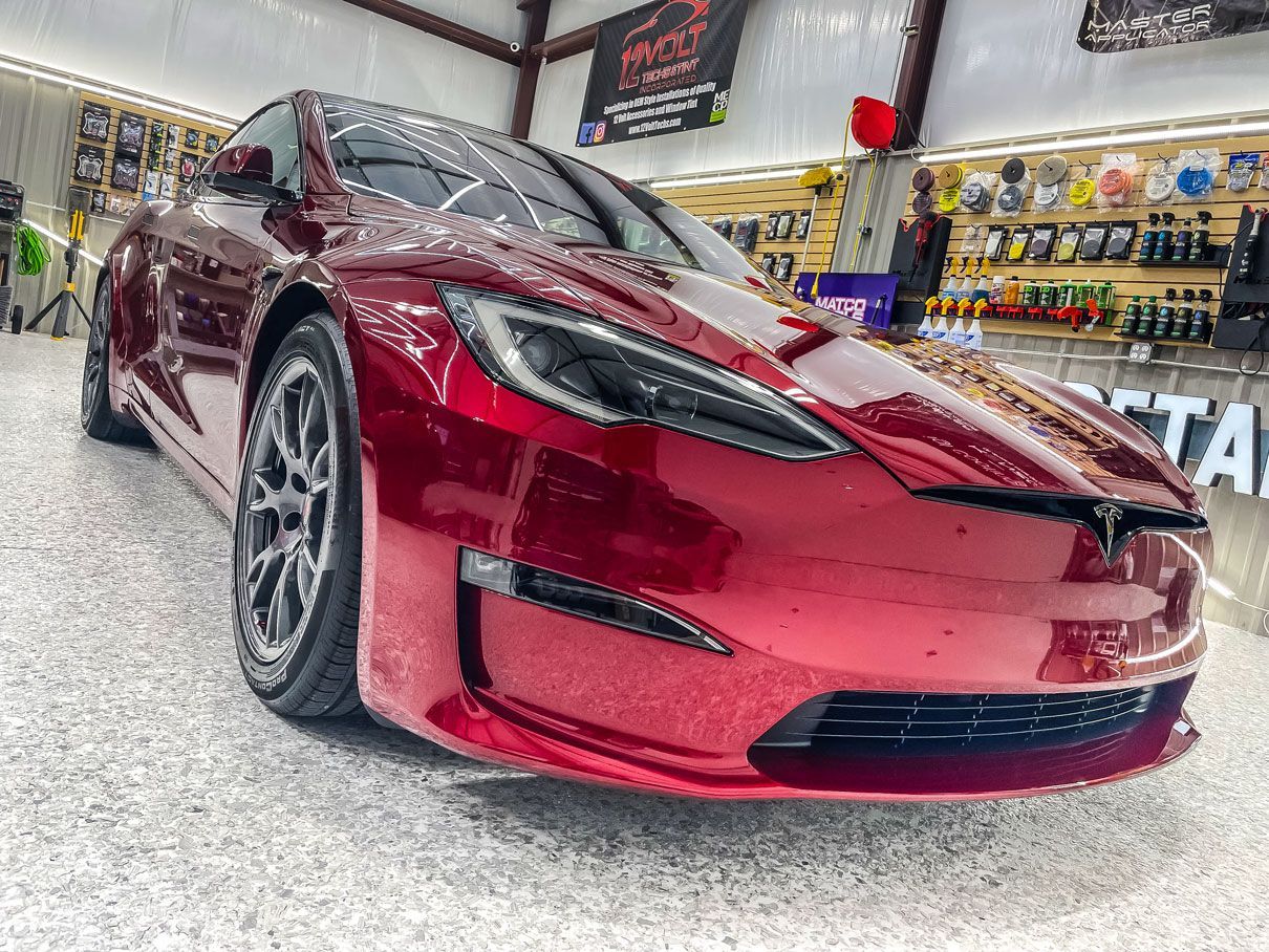 Red Tesla sedan in a garage, front view with glossy burgundy finish and custom wheels.