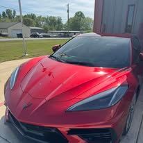 Red sports car with a shiny hood parked beside a building on a sunny day