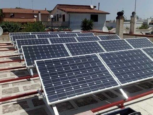 Pannelli solari installati su un tetto. Pannelli blu con bordi bianchi, montati su binari rossi, contro un cielo soleggiato.