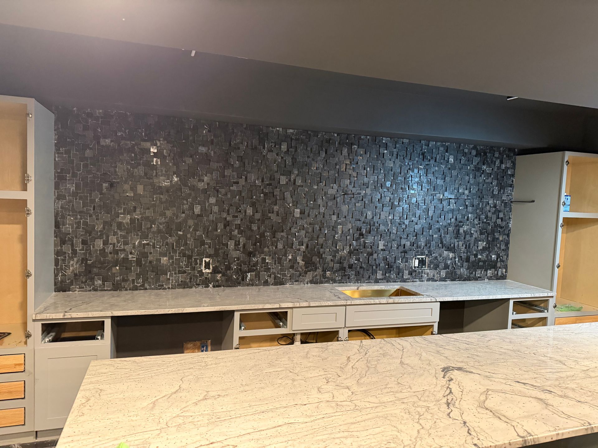Modern kitchen with a dark stone backsplash, white cabinets, and a light countertop under construction