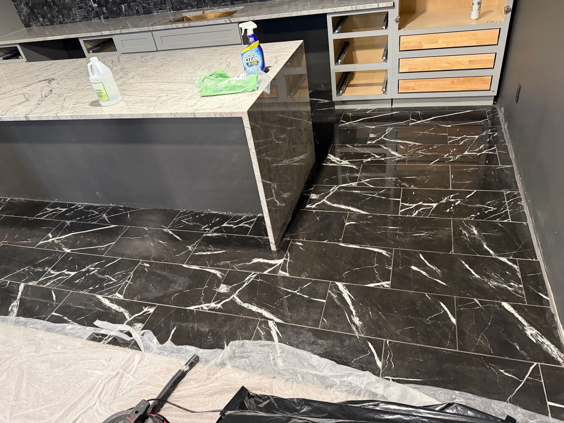 Modern kitchen under construction with black marble-look floor, gray island, and cleaning supplies on the counter
