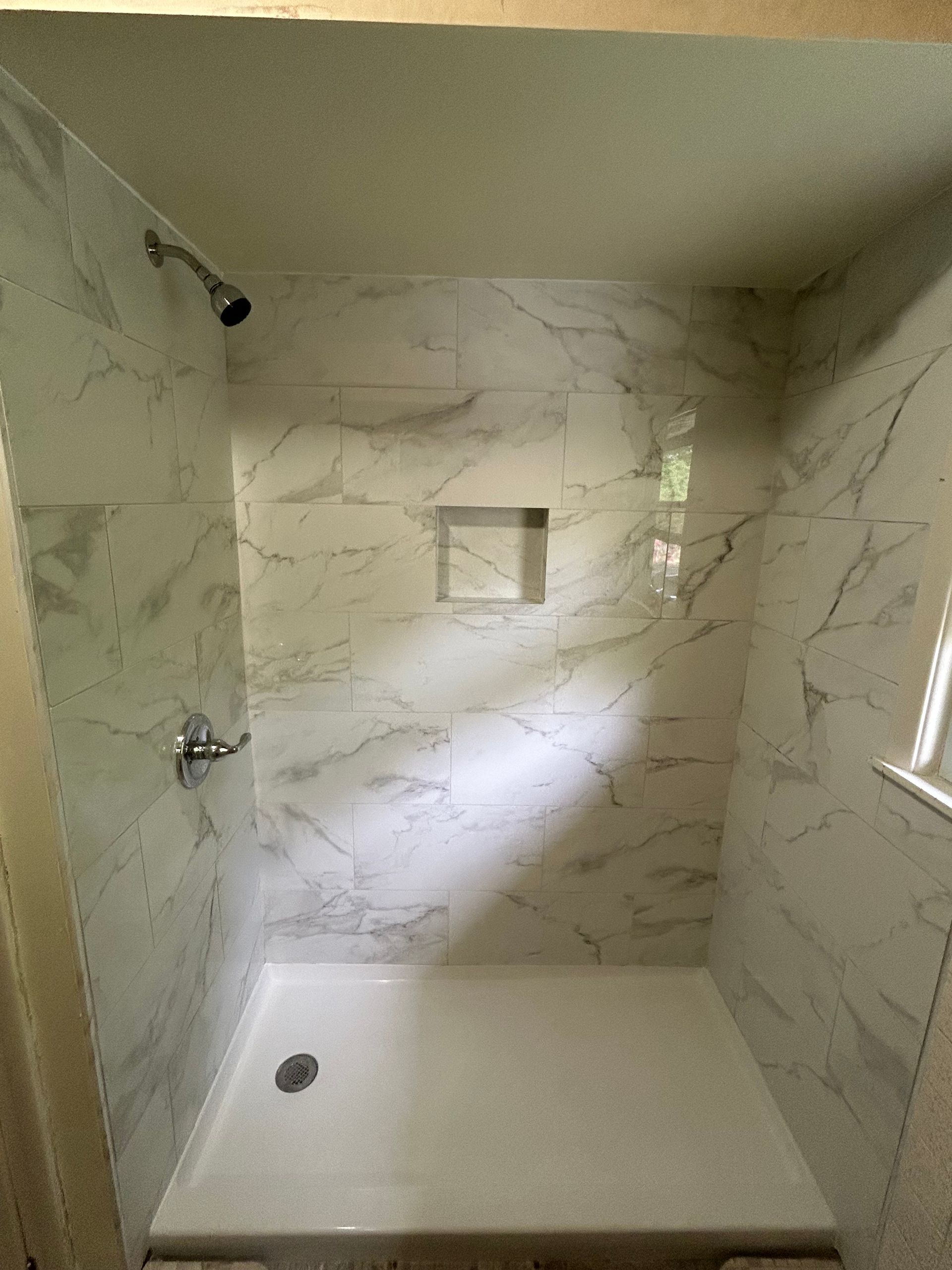 Empty tiled shower stall with built-in niche, white floor pan, and small window.