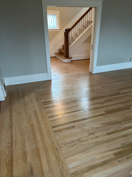 Empty room with hardwood floors, gray walls, white trim, and a doorway to a staircase.