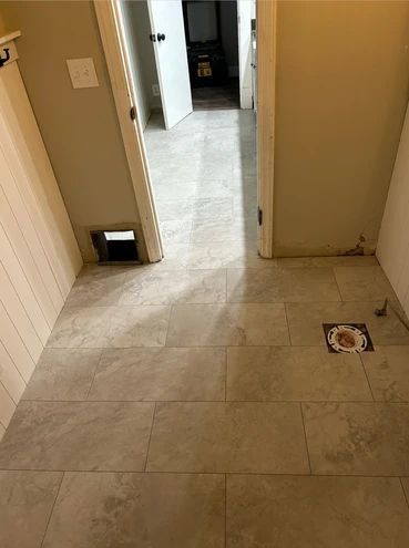 Tiled hallway with beige walls, a doorway ahead, and a floor drain on the right.