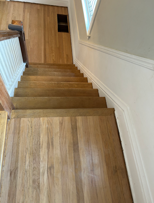 Wooden staircase with white railing and walls, viewed from the top landing indoors