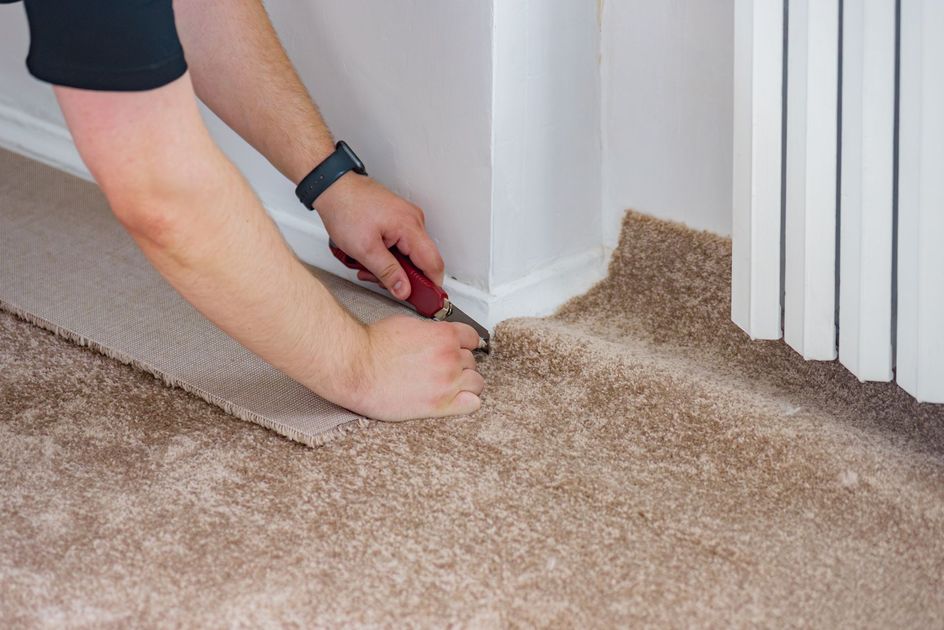 Person trimming beige carpet edges with a utility knife near a white wall and door frame