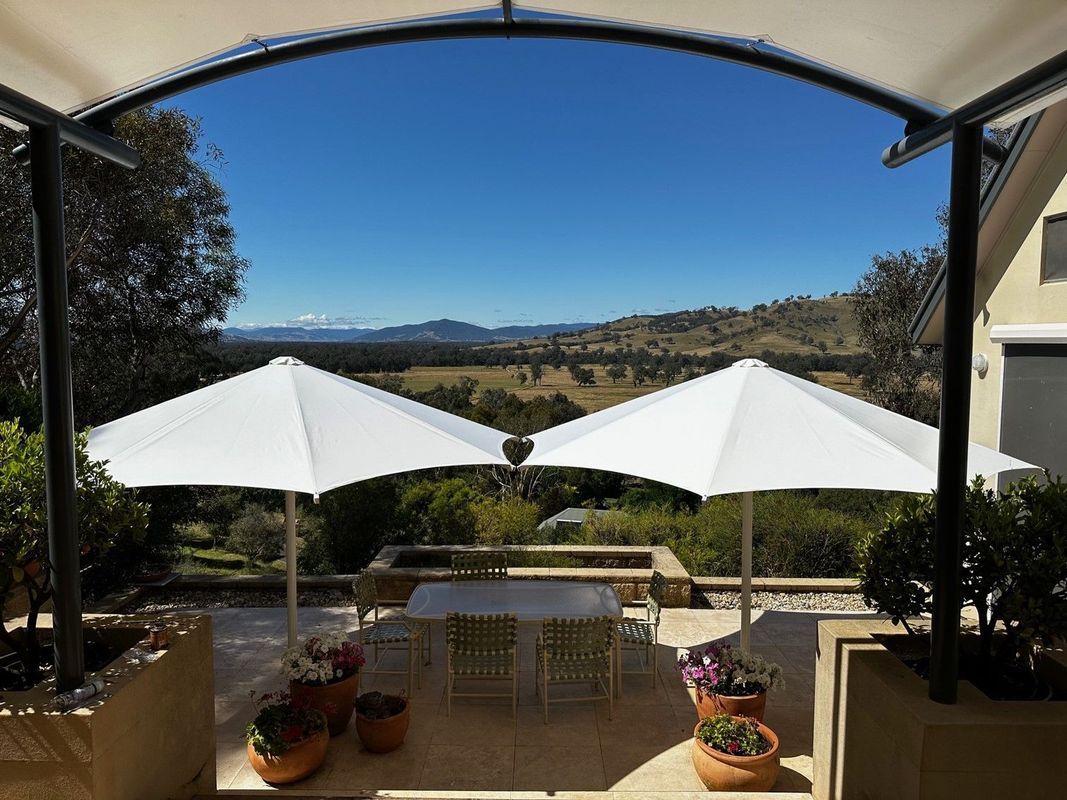 A Patio With a Dining Set and Two White Umbrellas Overlooking a Sunny — The Gazebo and Shade Centre in Jindera, NSW