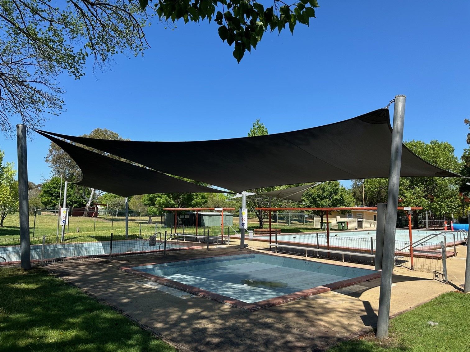 Shaded outdoor pool with black canopy, blue water, and lounge area under trees — The Gazebo and Shade Centre in Bright, VIC