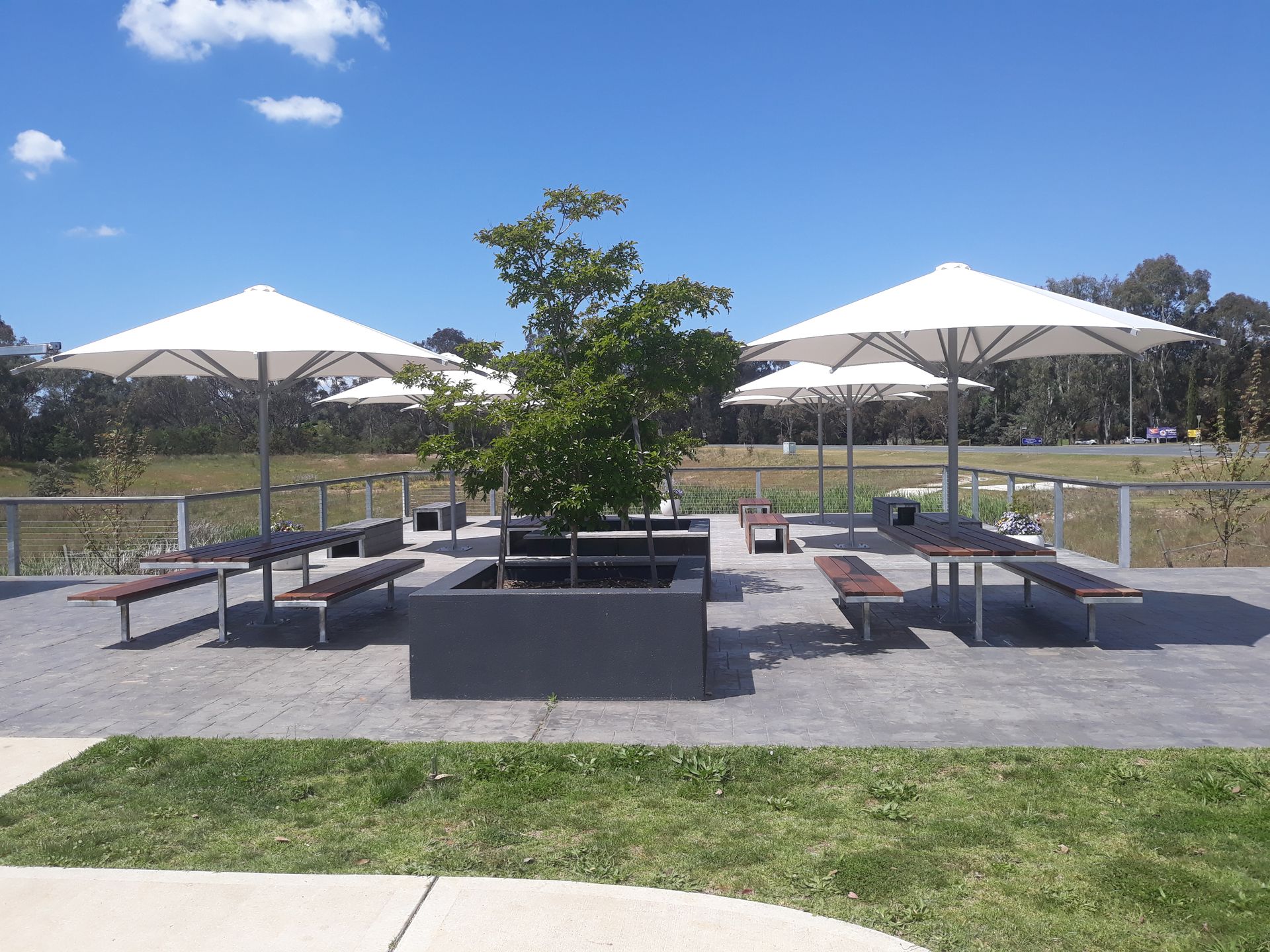 Outdoor patio with white umbrellas, benches, and a central planter under a blue sky — The Gazebo and Shade Centre in Wodonga, VIC