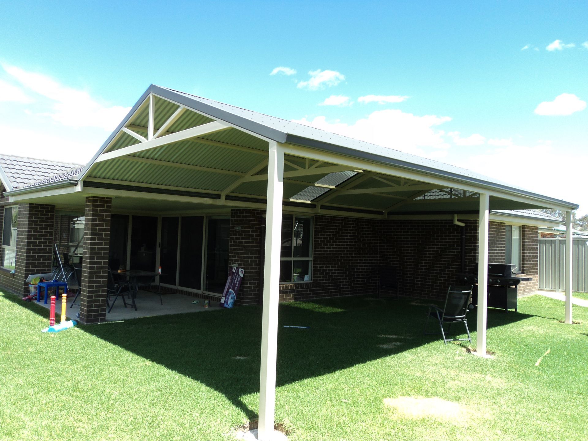 A Large Metal Patio Cover With a Gabled Roof Attached to a Brick House — The Gazebo and Shade Centre in Jindera, NSW