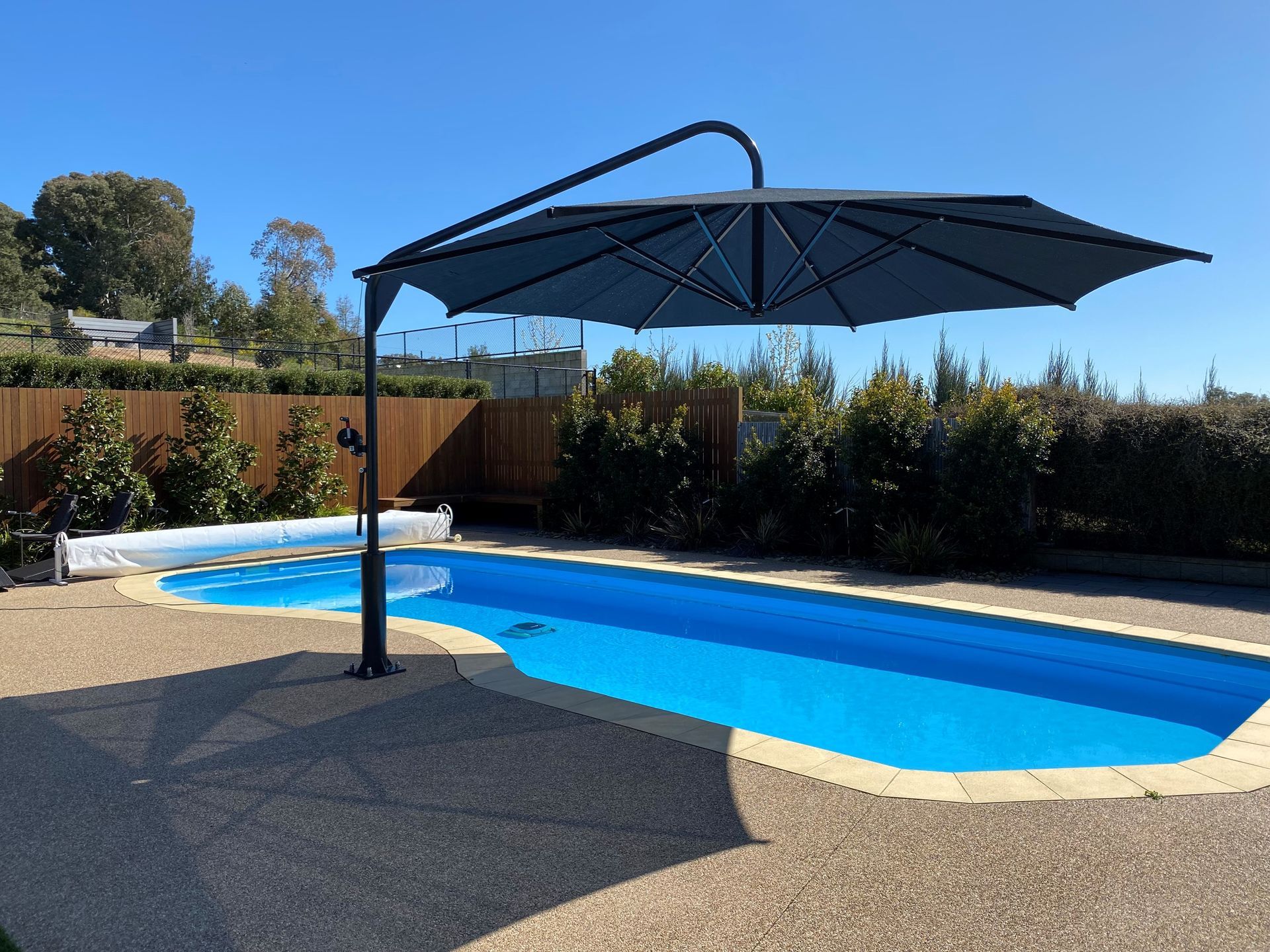 Backyard pool with a large black umbrella and blue water under a sunny sky - The Gazebo and Shade Centre in Wangaratta, VIC