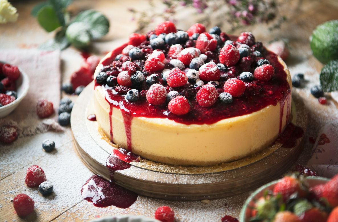 Berry-topped cheesecake on a rustic table, drizzled with red sauce and surrounded by scattered berries Berry-topped cheesecake on a rustic table, drizzled with red sauce and surrounded by scattered berries