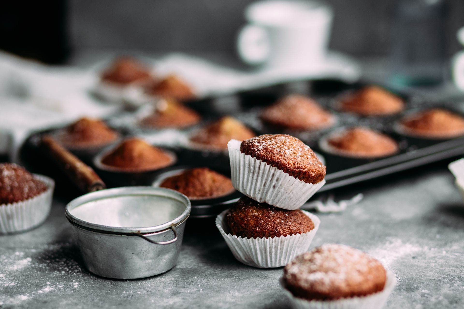 Chocolate muffins in paper cups on a baking tray dusted with flour, with a metal measuring cup in front