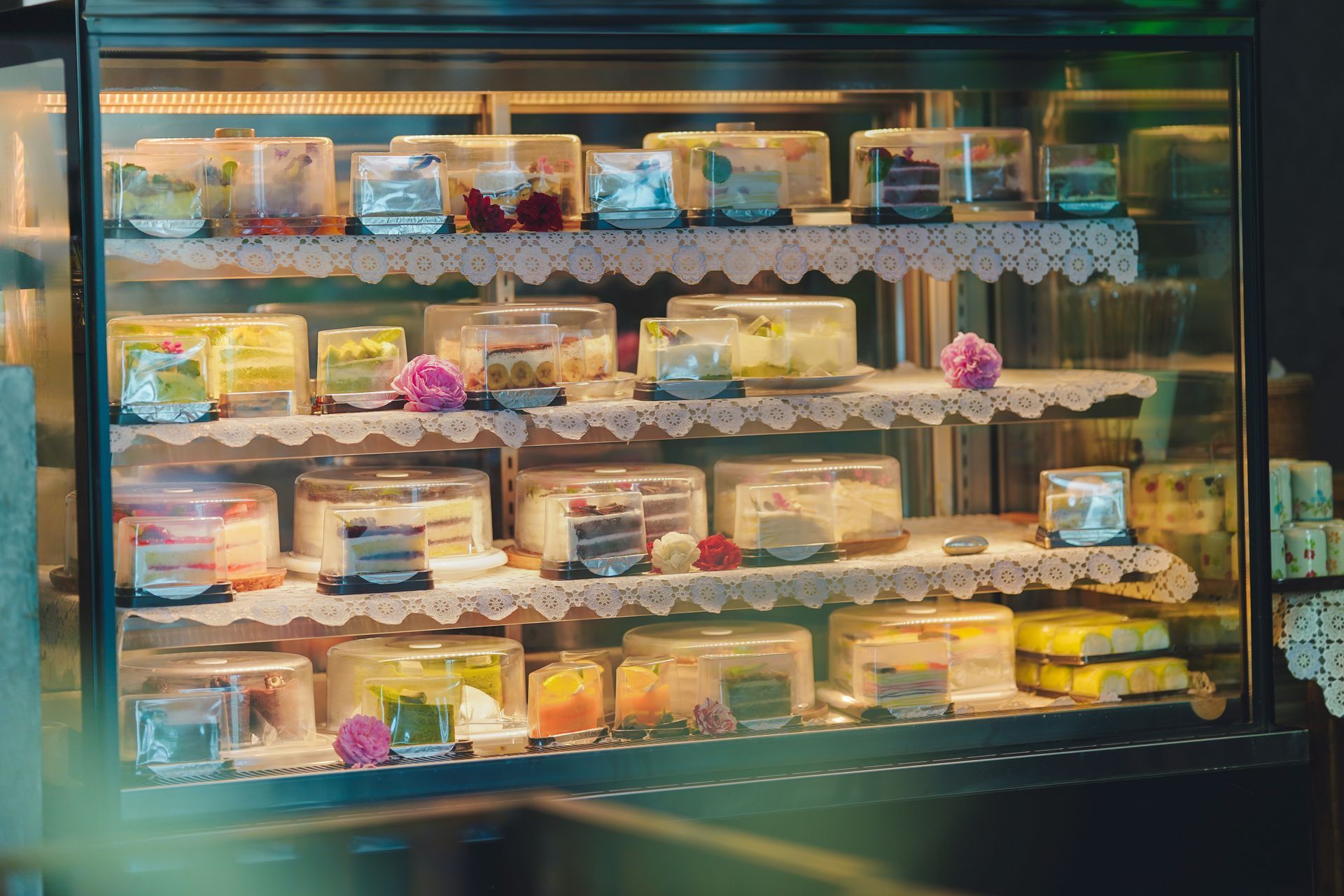 Bakery display case filled with assorted cakes, pastries, and colorful desserts on lit shelves