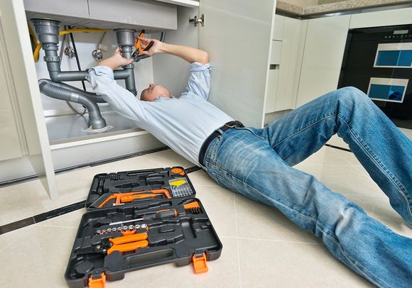 Man Repairing Sink Pipe in the Kitchen — El Paso, TX — Plumbers Drain Cleaning Man Repairing Sink Pipe in the Kitchen — El Paso, TX — Plumbers Drain Cleaning