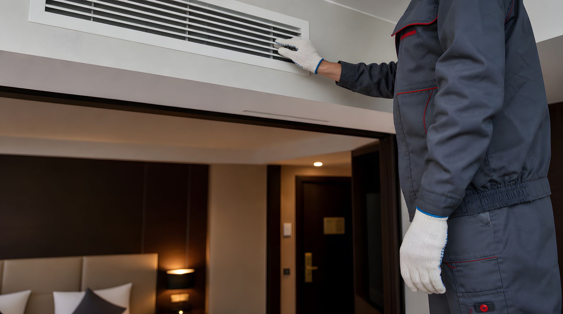 Technician in gray uniform and white gloves inspecting a ceiling-mounted HVAC air vent and grille. Technician in gray uniform and white gloves inspecting a ceiling-mounted HVAC air vent and grille.