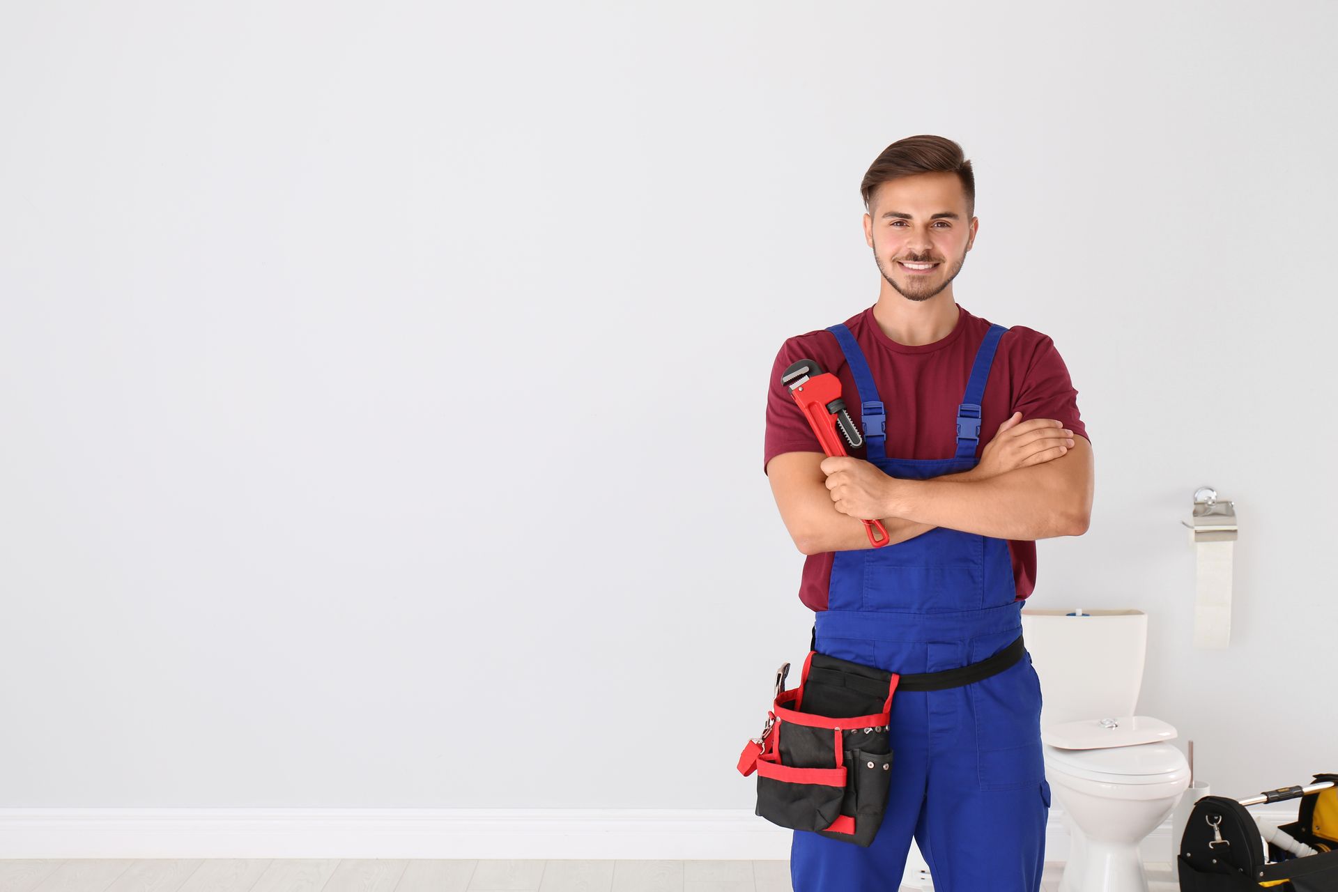 Young man with plumber wrench and toilet bowl on background. Young man with plumber wrench and toilet bowl on background.