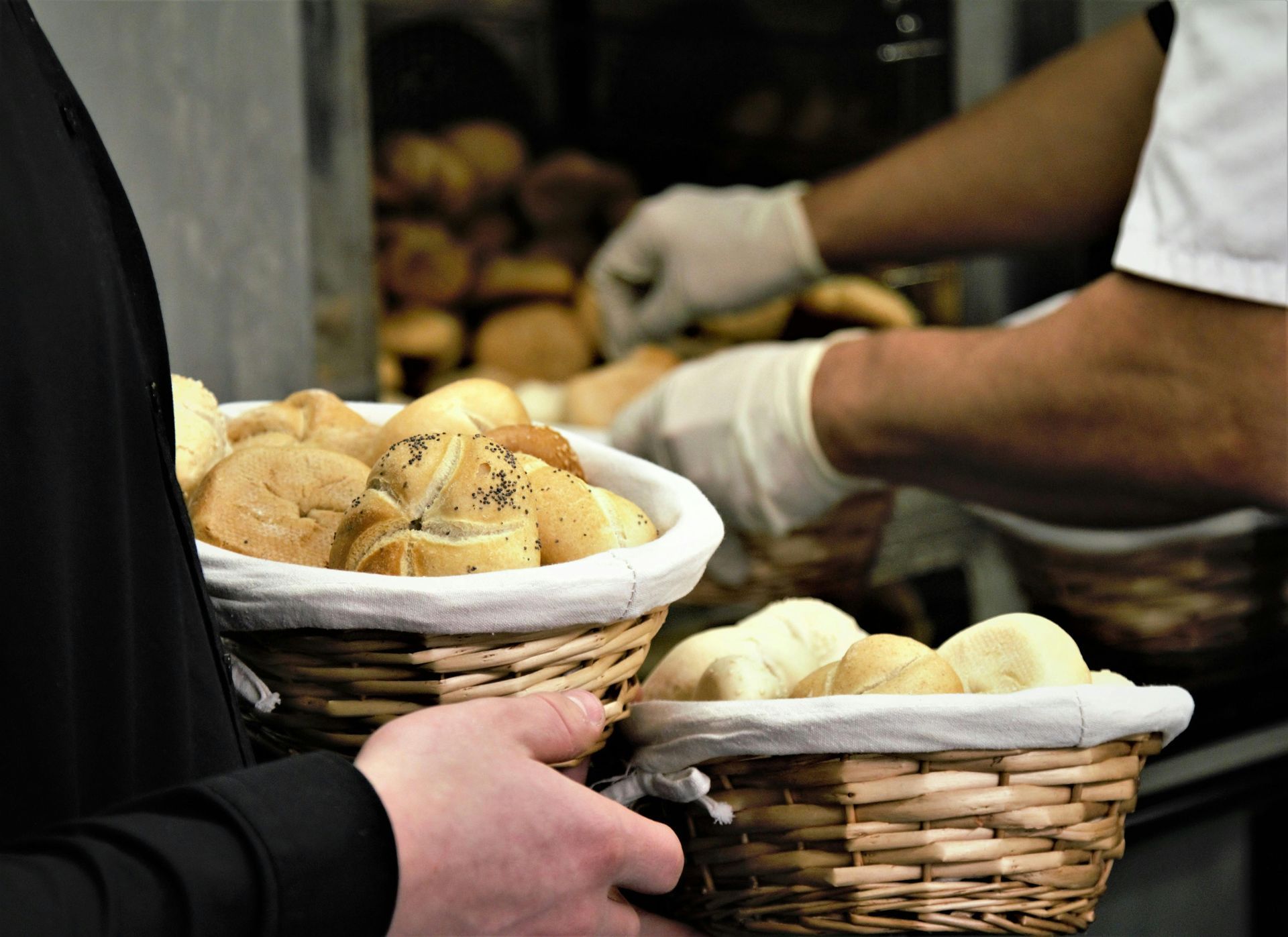 Hands holding baskets of bread being served at a market or bakery counter
