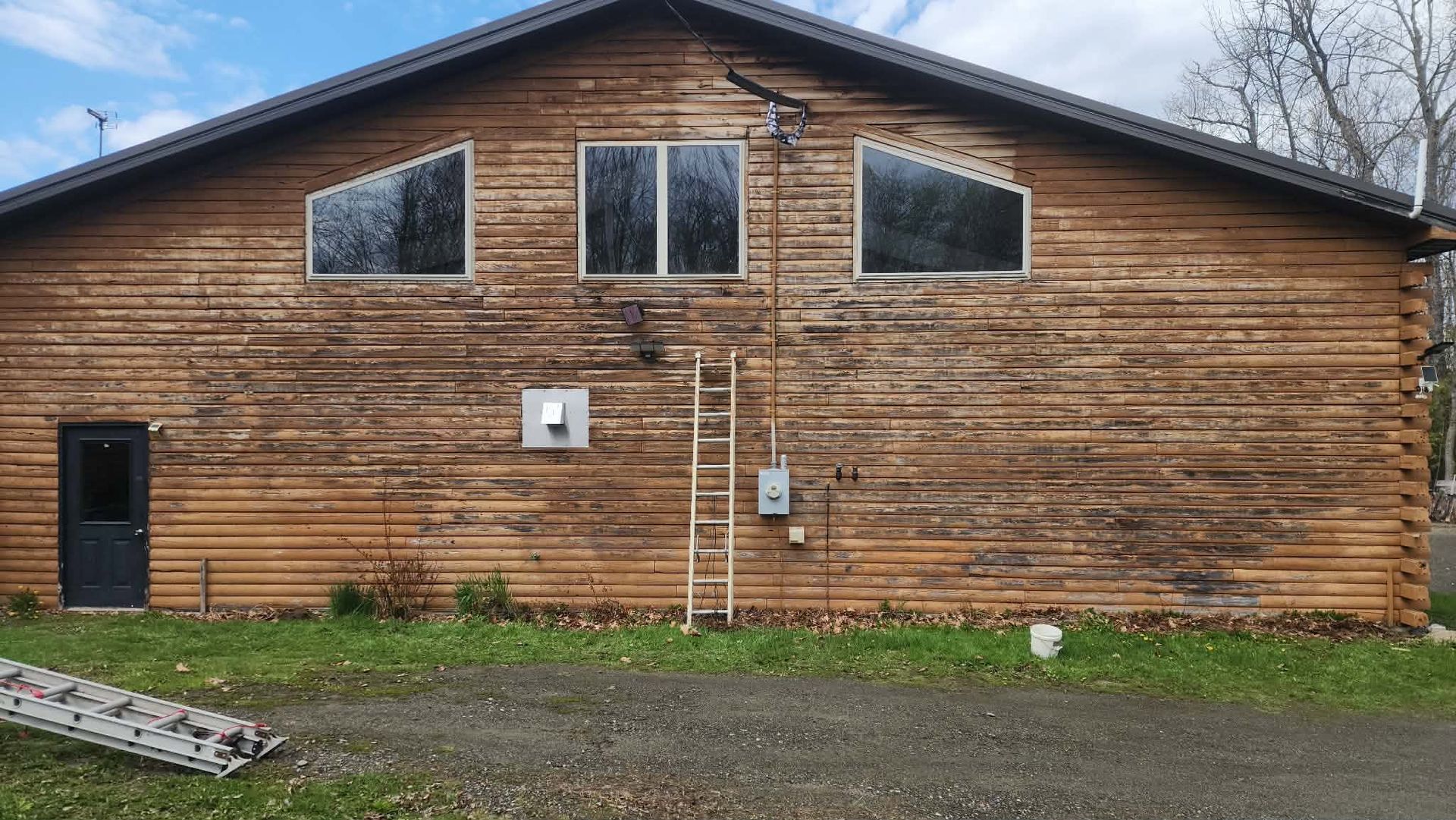 Weathered wooden building with three windows and two doors, seen from the outside on a gravel lot.