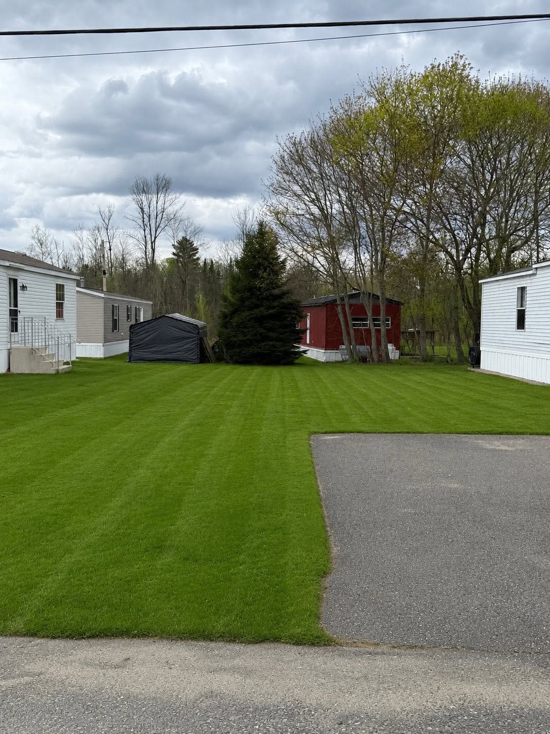 Grassy RV park with white trailers, a red shed, and cloudy sky