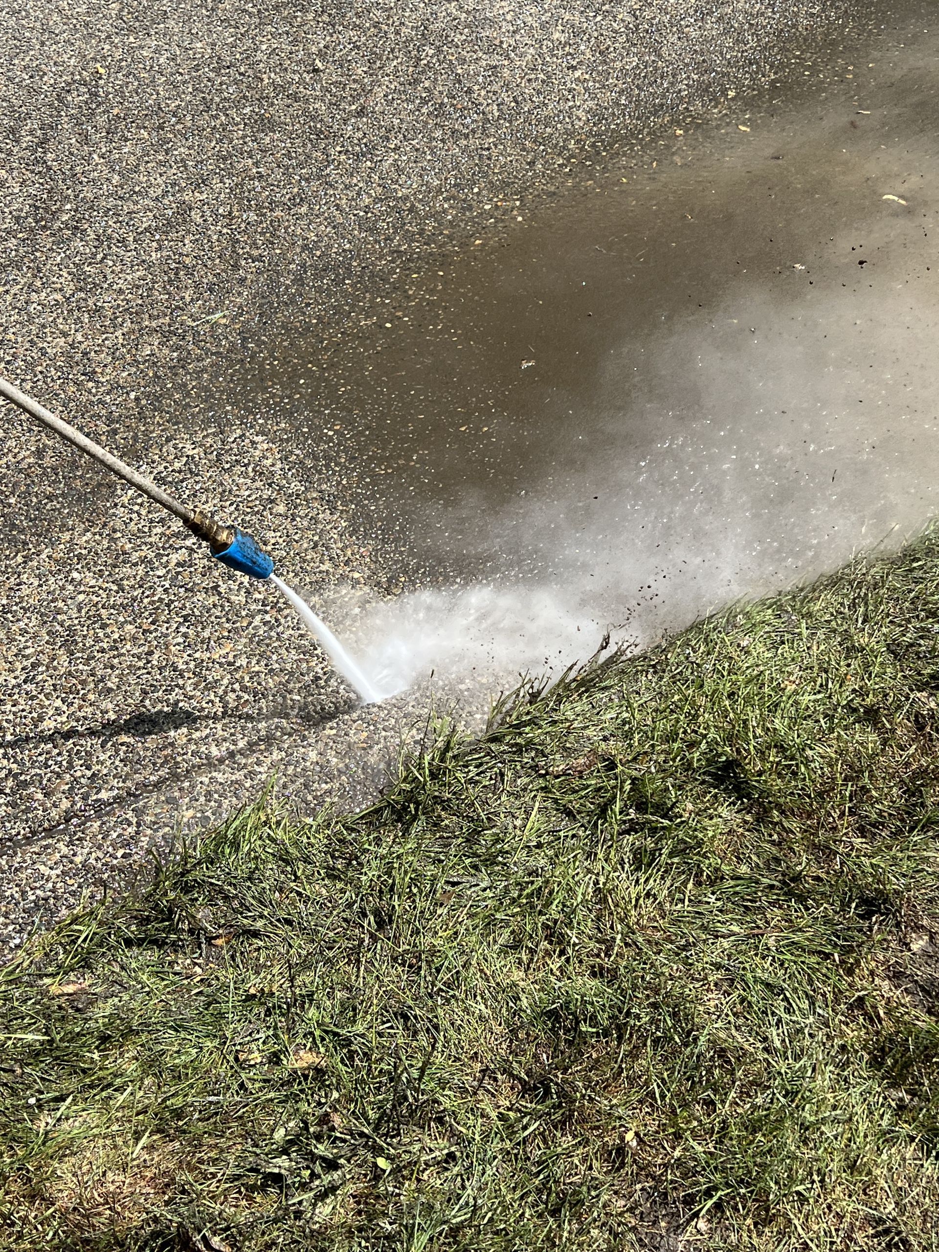 Blue hose spraying water onto a concrete surface beside grass and pavement