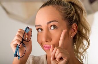 A woman is holding a pair of glasses and a pair of contact lenses.