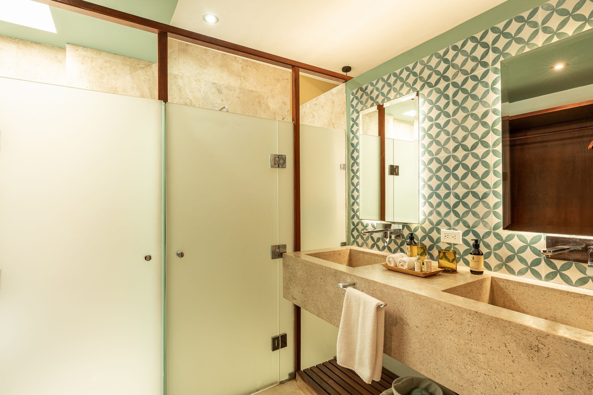 Bathroom with dual sinks, shower, patterned wall tiles, and wood accents.