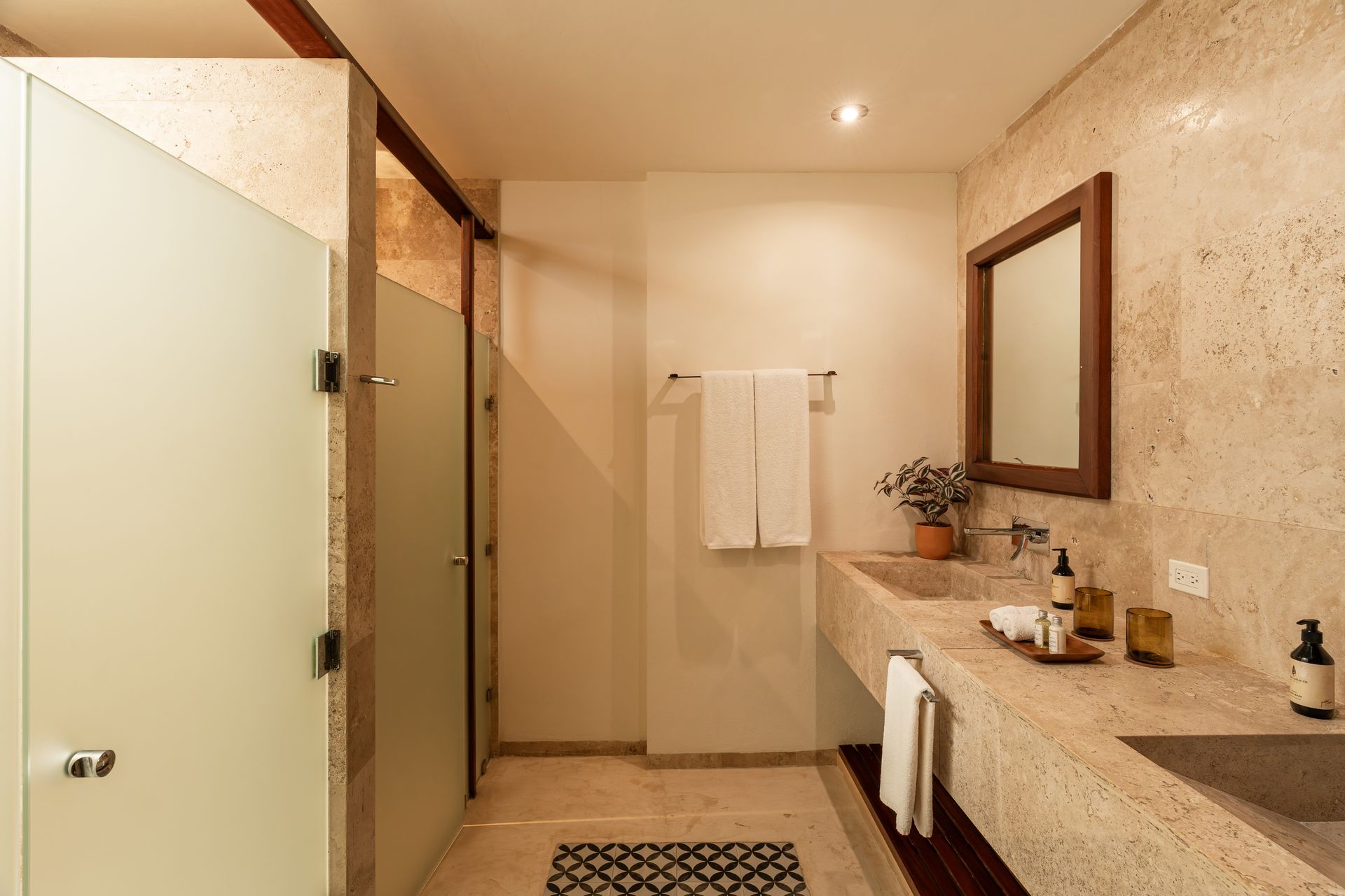 Bathroom with stone walls and countertop, glass shower door, wooden mirror frame, and towels.