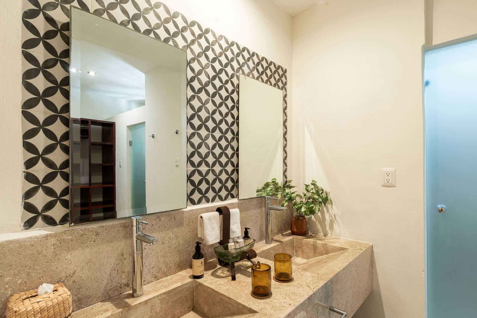 Bathroom with double sinks, patterned mirror frame, beige countertop, and frosted glass shower door.
