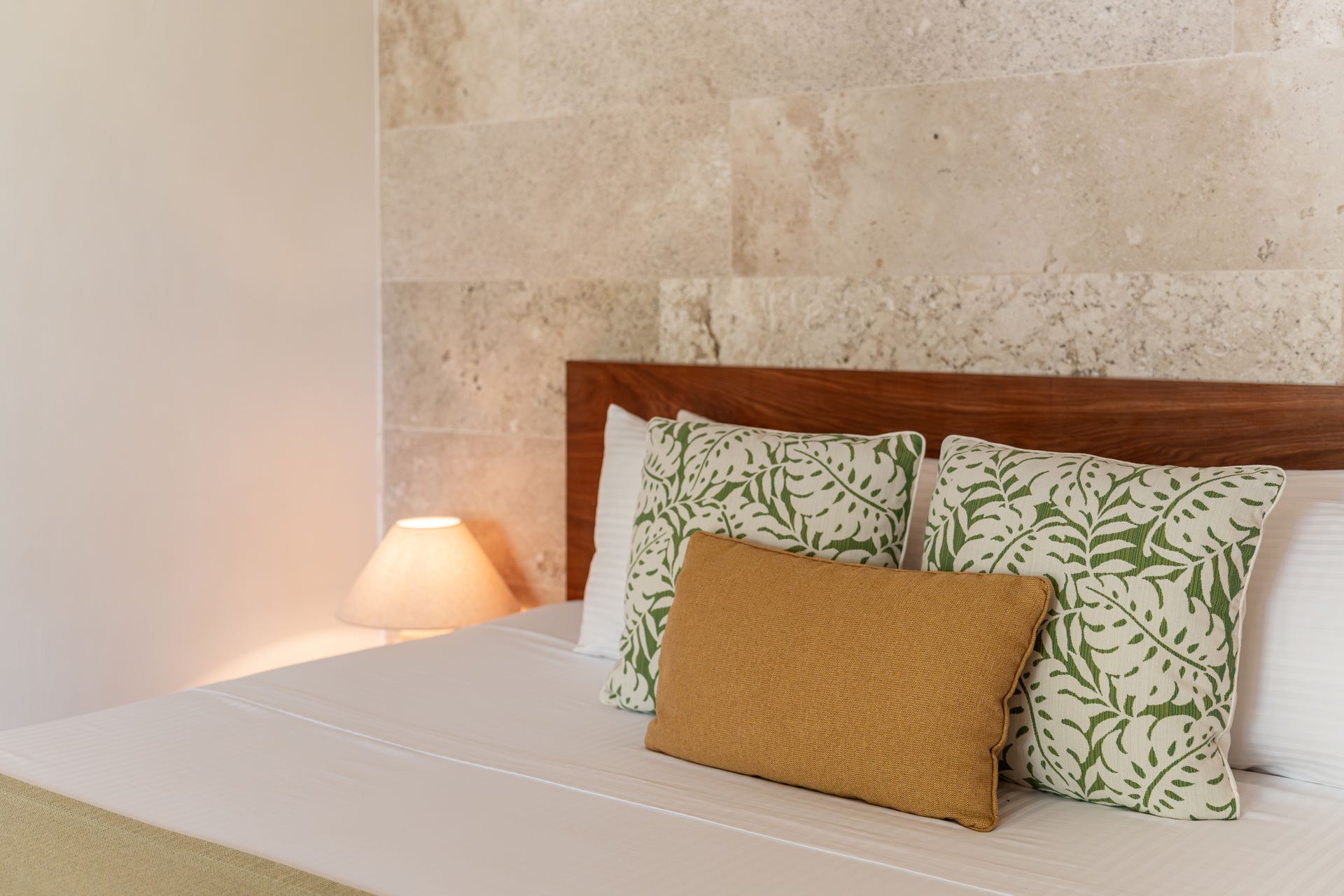 Bedroom with bed, pillows, and nightstand with lamp; textured wall in background.