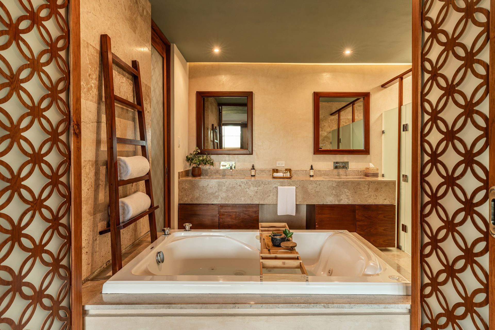 Bathroom with jacuzzi, towel rack, stone countertops, two mirrors, and decorative wood door.