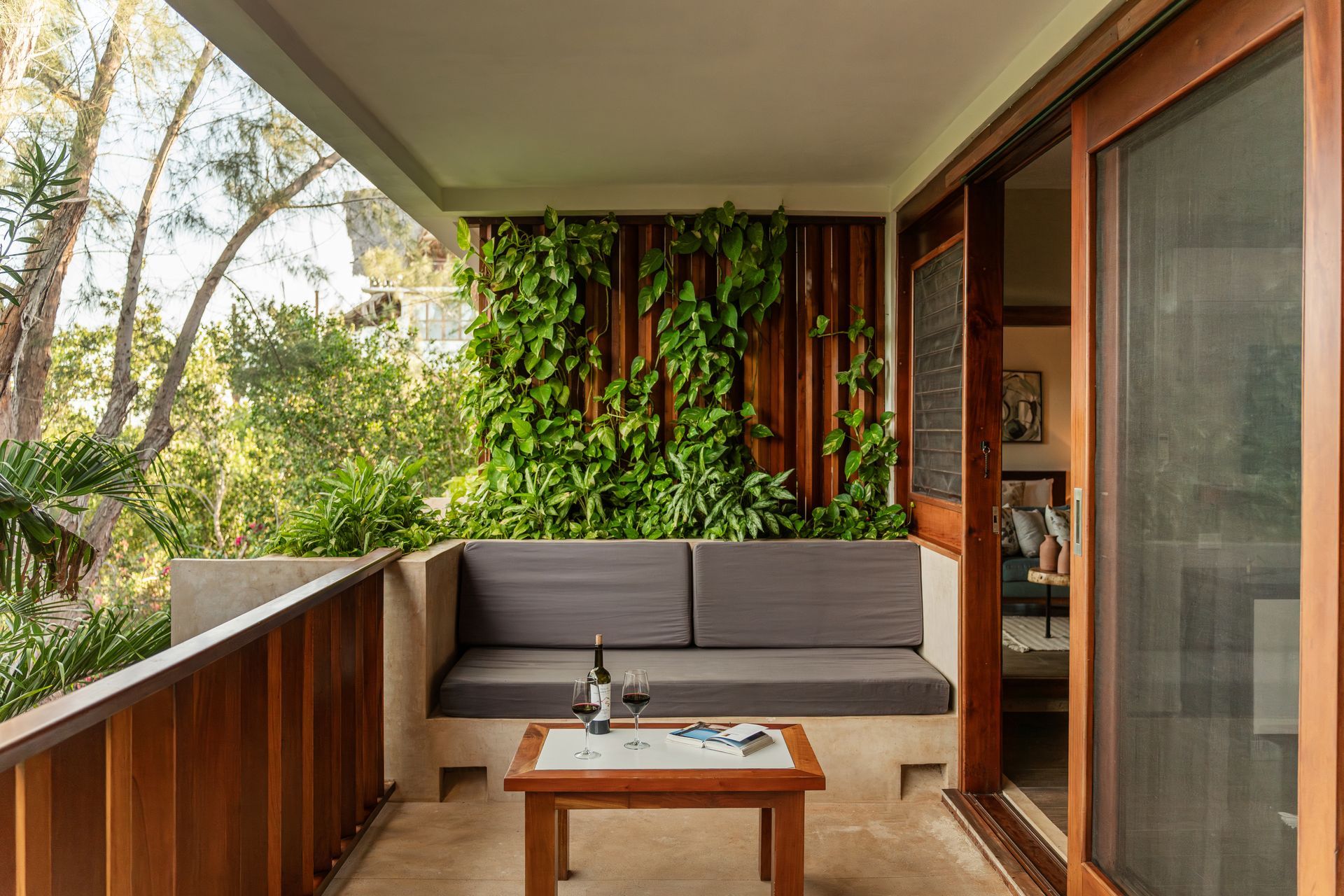 Balcony with wood accents, built-in sofa, coffee table with wine glasses, and a green wall with plants.