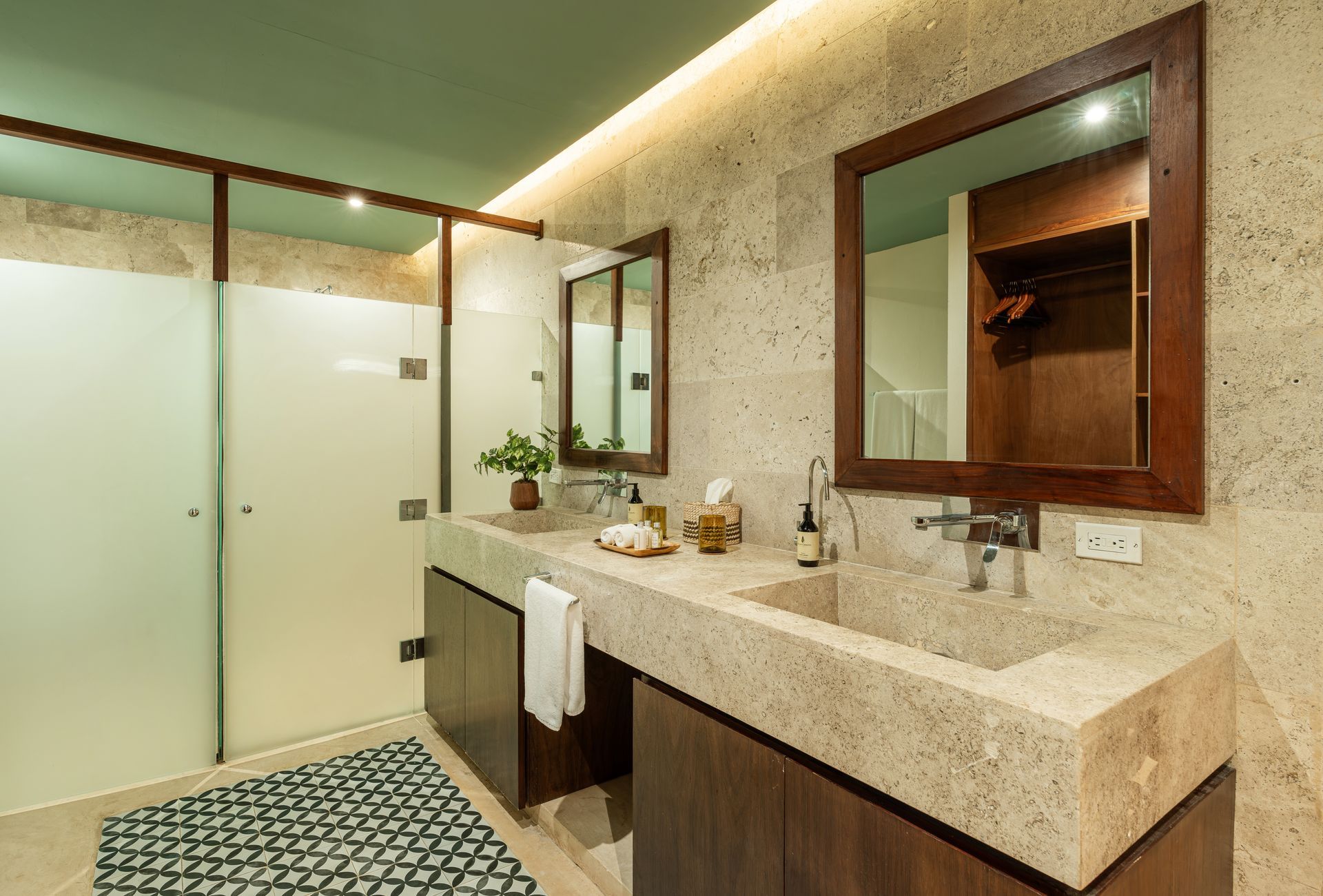 Modern bathroom with double sinks, speckled countertop, wooden cabinets, and frosted glass shower.