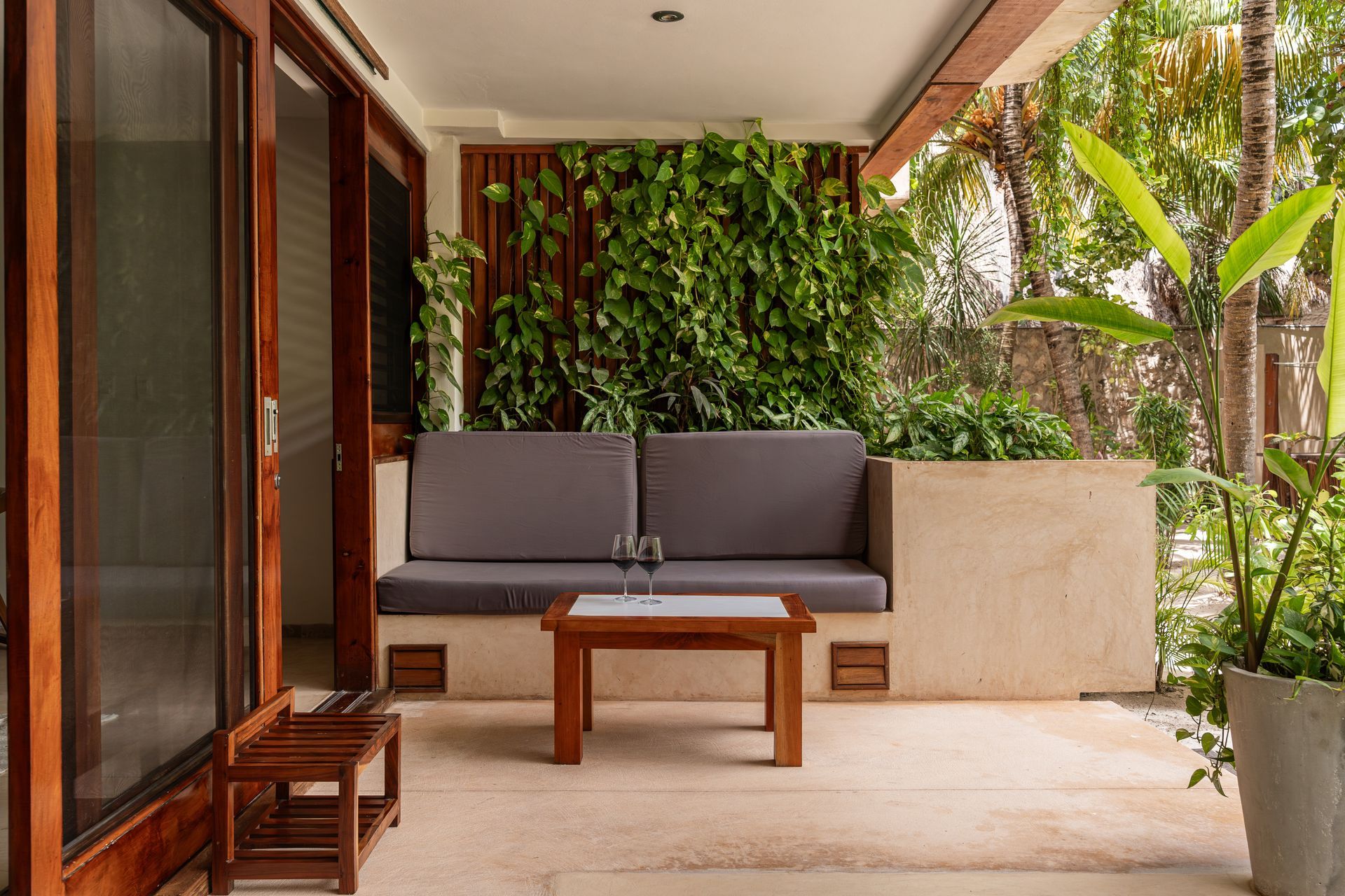 Outdoor seating area with gray sofa, wooden table, and lush green wall.