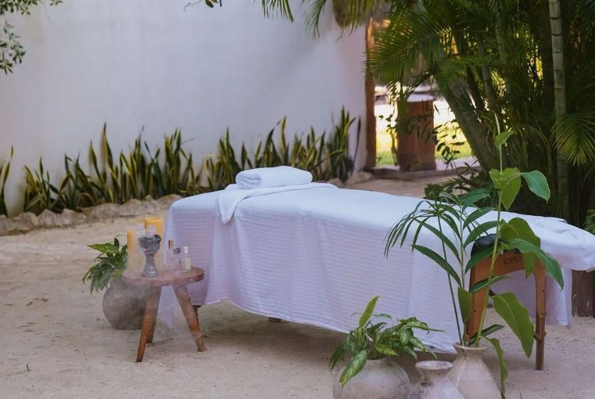 Spa massage table outdoors in a tropical garden, covered with a white sheet and surrounded by plants