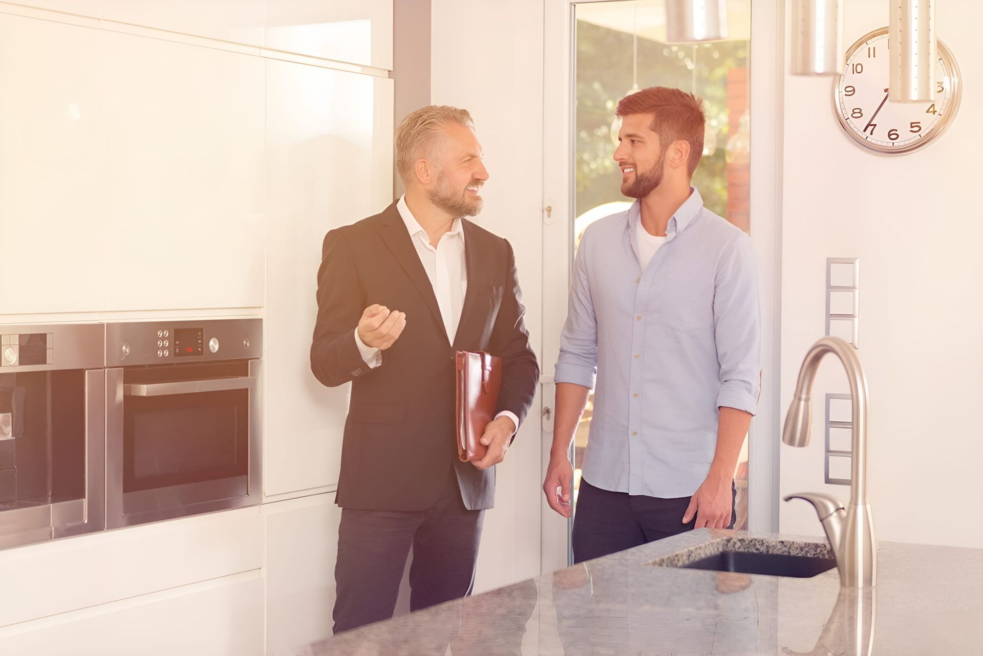 Two Men Are Standing In A Kitchen Talking To Each Other — North Coast Conveyancing In Port Macquarie, NSW