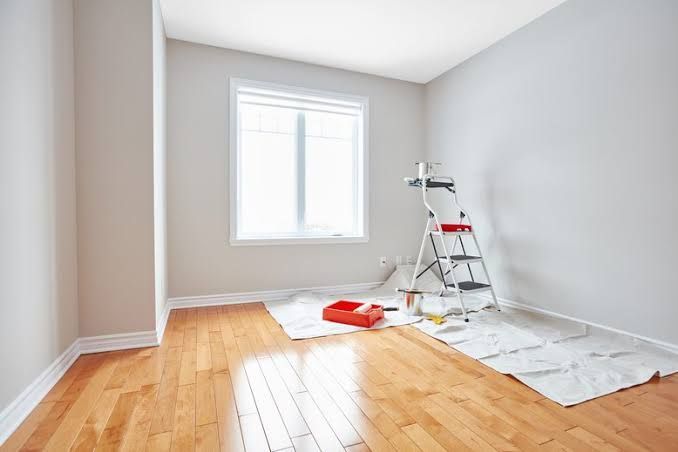 Freshly painted empty room with hardwood floor, window, ladder, and paint supplies