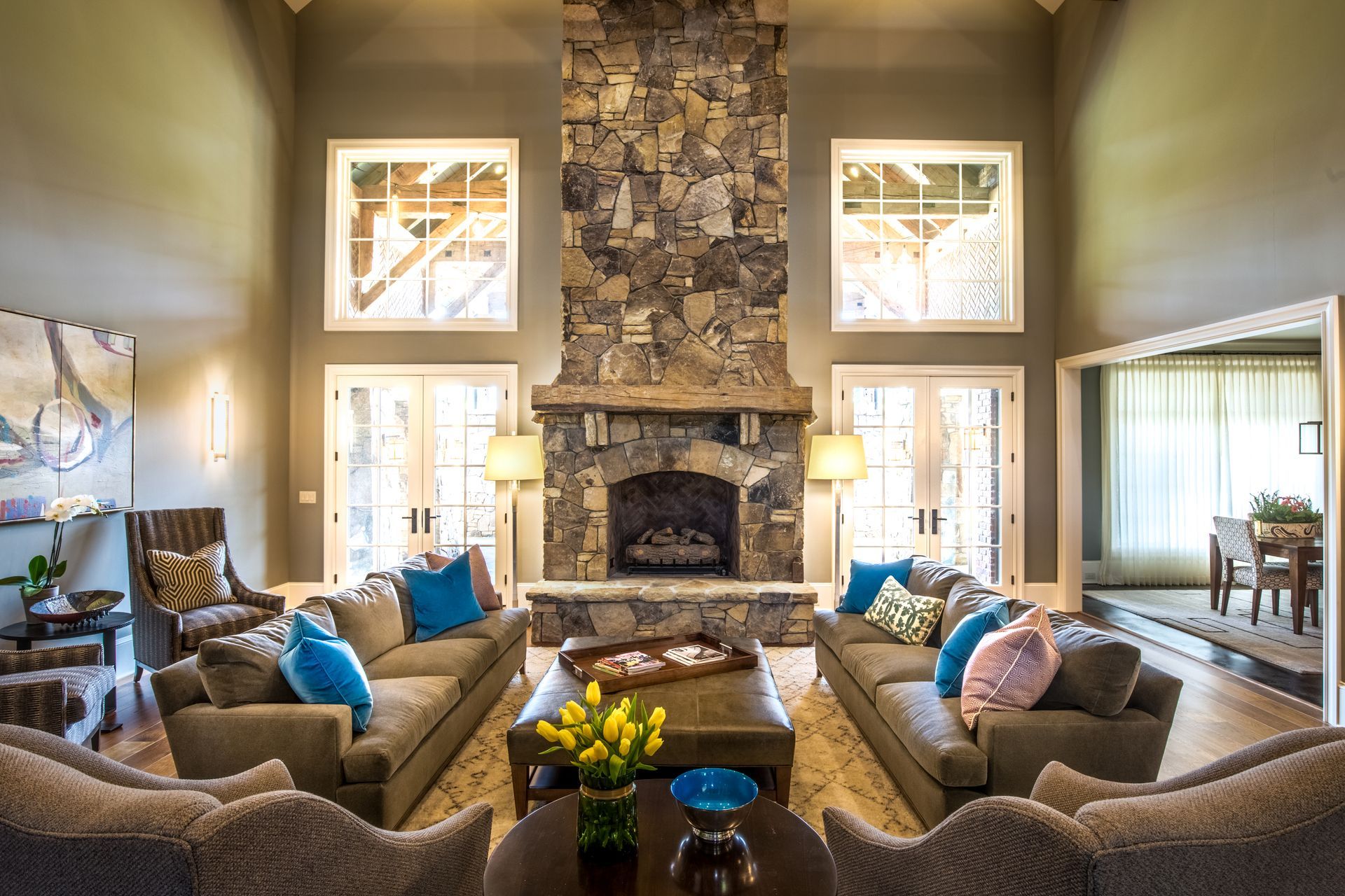 Living room with stone fireplace, sofas, large windows, and neutral color scheme.