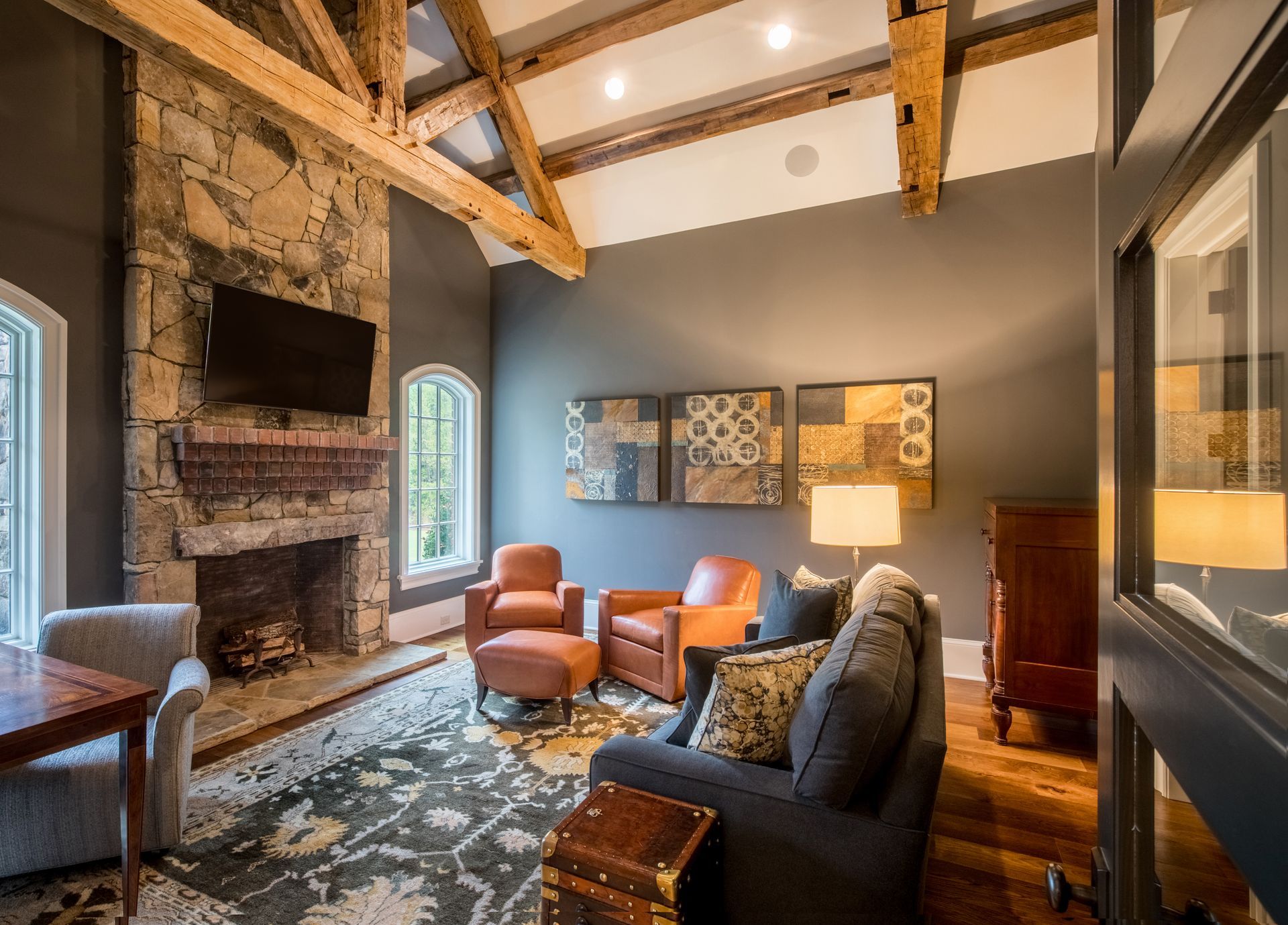 Living room with stone fireplace, wood beams, gray walls, and leather furniture.