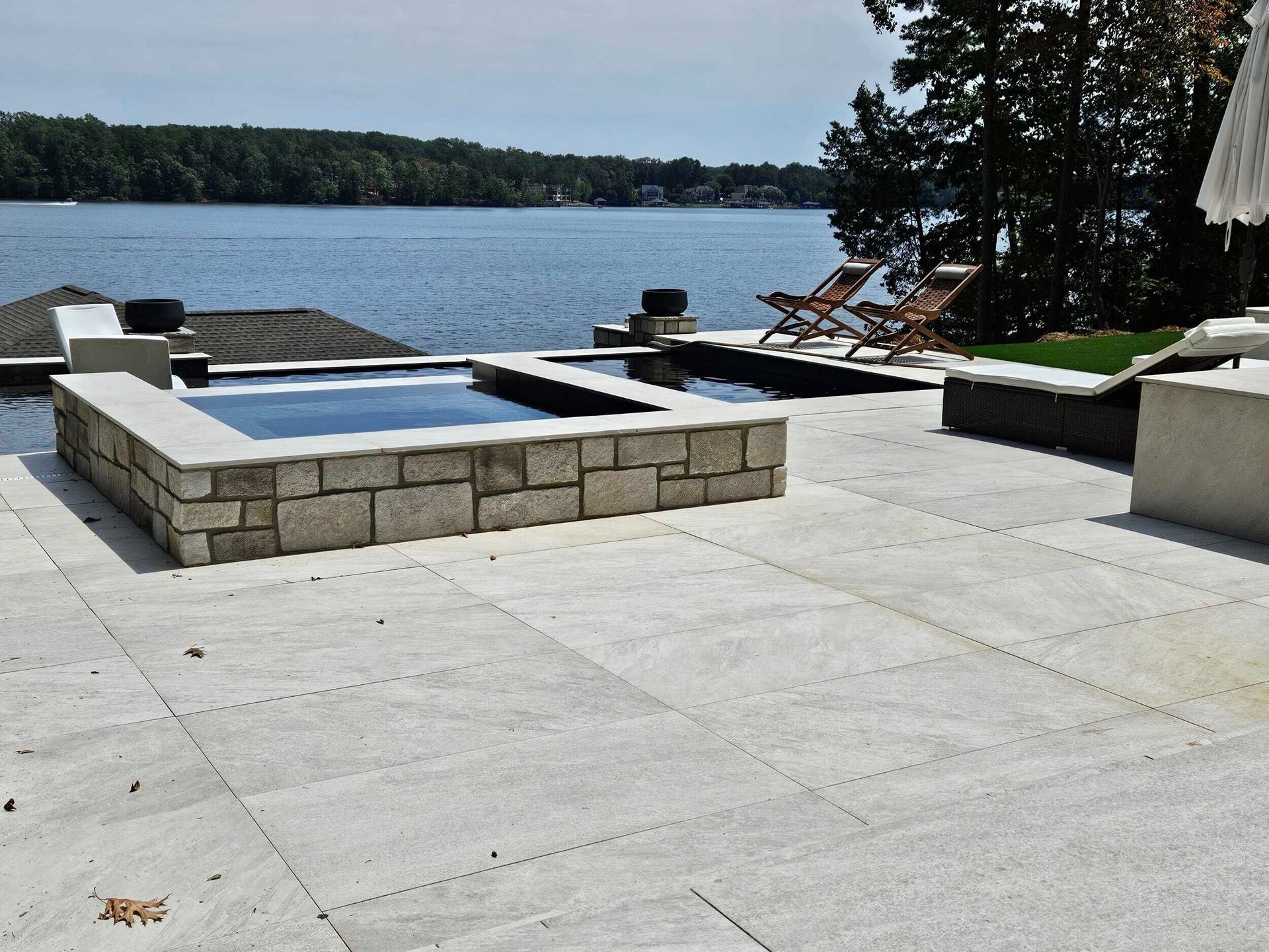 Patio with stone hot tubs and lounge chairs overlooking a lake.