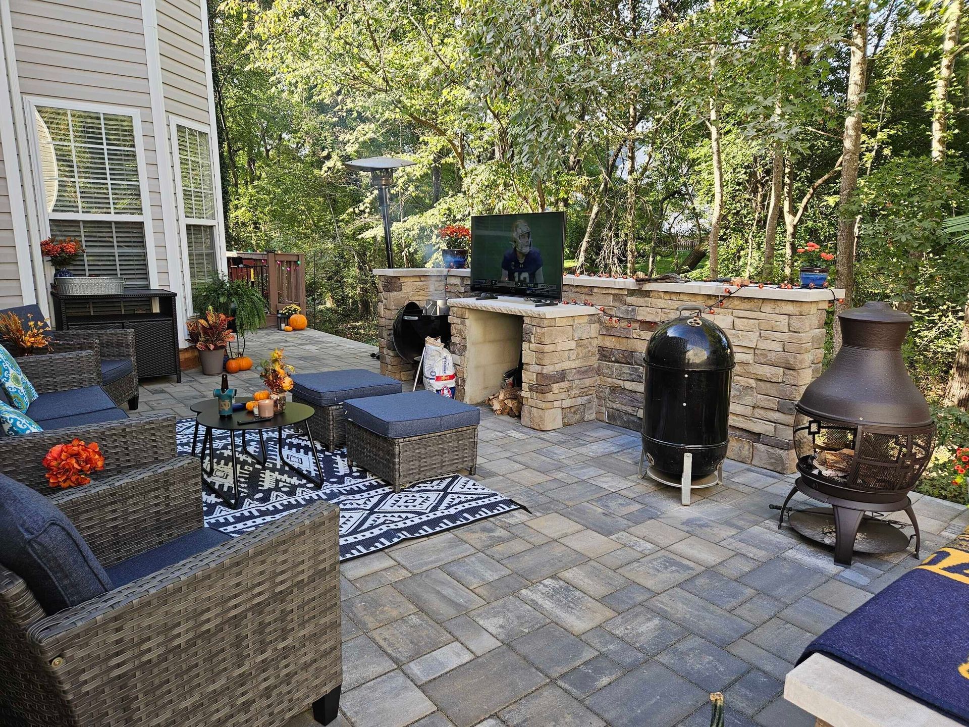 Outdoor patio with seating, stone fireplace, TV, grill, and decorative fire pit.