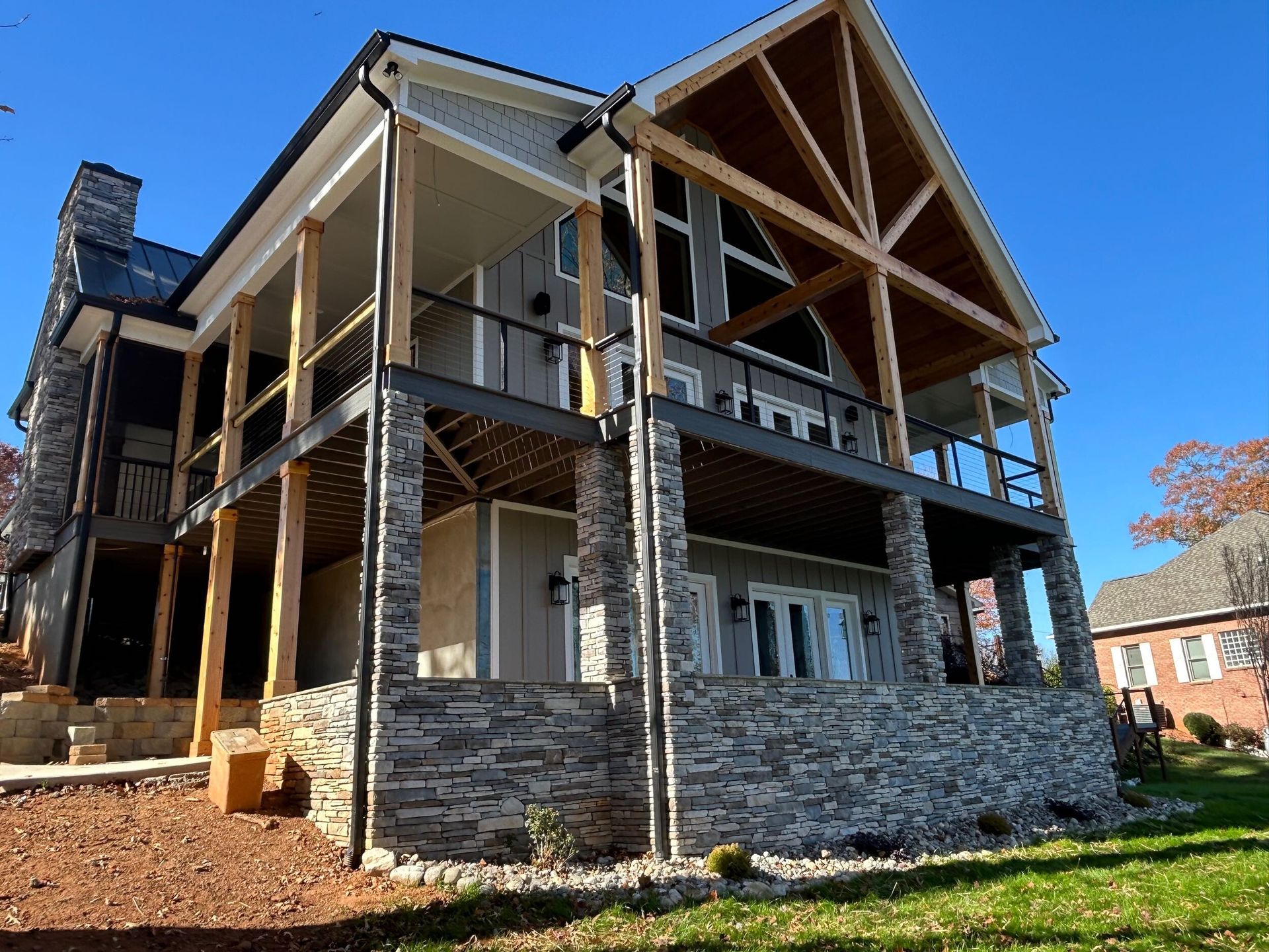 A two-story house with a large stone foundation, a wooden deck, and a prominent gable roof, set under a clear blue sky.