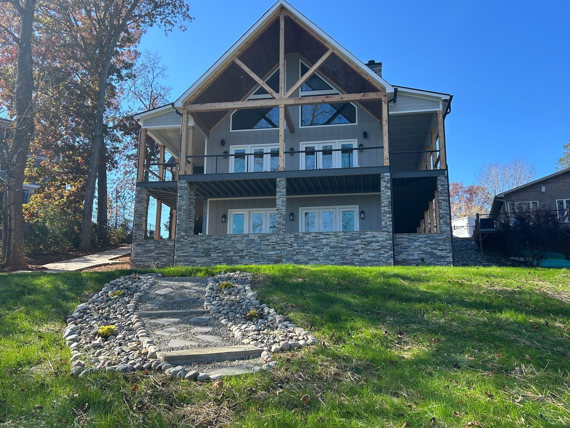A large, two-story house with stone masonry and a covered porch faces a grassy yard with a stone-lined walkway.