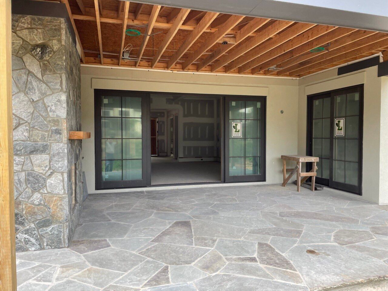 Patio with stone floor, open sliding doors, exposed wooden ceiling, and stone wall on the left.